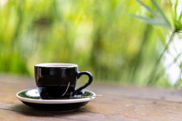 espresso coffee with in the black cup on wooden table with blur tree background