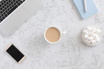 Modern and fashion office desk with laptop, blue notebook, mobile phone, pen, marshmallows and coffee cup, flat lay. Top view of female table with copy space