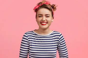People and happiness concept. Adorable young smiling female dressed in sailor sweater, being pleased by pleasant story, stands against pink background. Joyful pinup girl expresses positiveness - obrazy, fototapety, plakaty