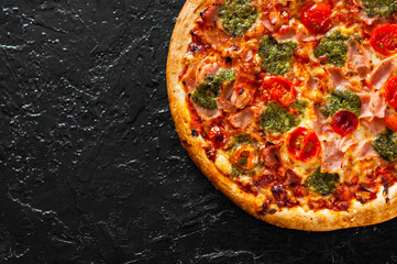 Pizza with Mozzarella cheese, Ham, Tomatoes, pepper, Spices and Fresh Basil pesto sauce. Italian pizza.on black background. with copy space. top view