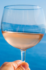 Woman's hand holding a glass of rose wine with the seaside in the background.  Taken in Italy 