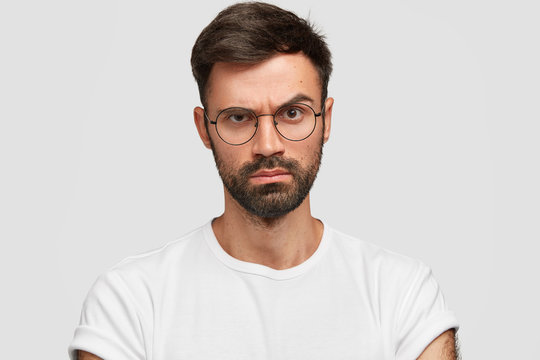 Strict serious discontent male boss raises eyebrows with angry displeased expression, dislikes something, expresses negative emotions, dressed casually, poses against white studio background.