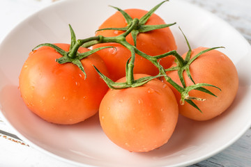 Four tomatoes still connected to the vine in a white bowl in a bright and airy setting
