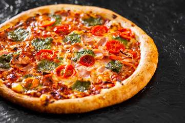 Pizza with Mozzarella cheese, Ham, Tomatoes, pepper, Spices and Fresh Basil pesto sauce. Italian pizza.on black background.
