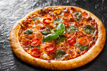 Pizza with Mozzarella cheese, Ham, Tomatoes, pepper, Spices and Fresh Basil pesto sauce. Italian pizza.on black background.