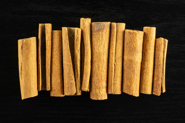 Lot of whole dry brown cinnamon stick in line flatlay on black wood