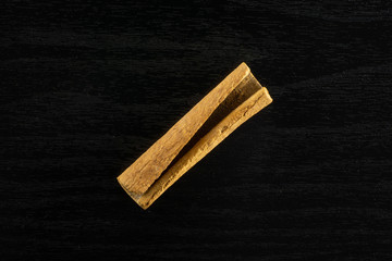 One whole dry brown cinnamon stick flatlay on black wood