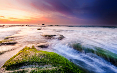 colorful sunset seascape with natural coastal rocks on the ground. soft focus due to slow shutter and water movement.