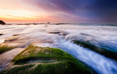 colorful sunset seascape with natural coastal rocks on the ground. soft focus due to slow shutter and water movement.