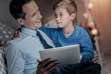 Be positive. Cheerful male person keeping smile on face while looking at his kid