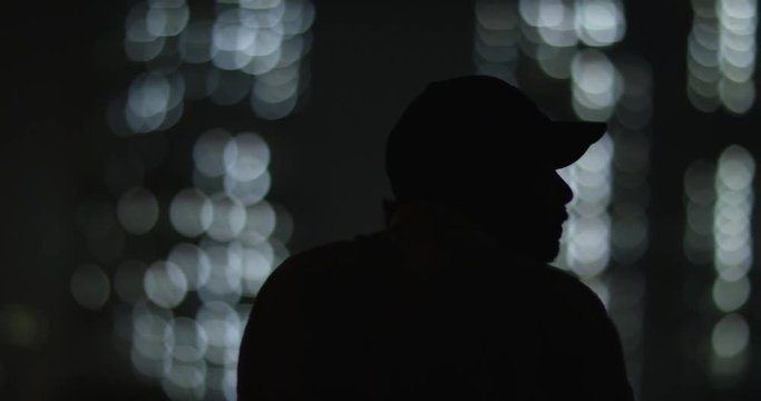 Man in silhouette looking out over city. Background has lights from sky scrapers. Beautiful, two toned lights. Slow motion.