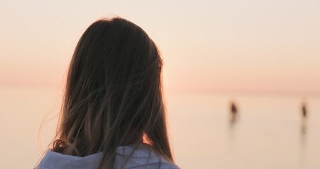 teenage girl standing on a beach at sunset shot from behind