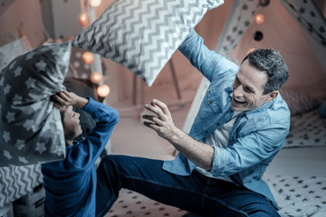 Lets play. Happy male person laughing while playing with his son