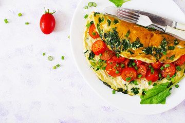 Omelette with tomatoes, spinach and green onion on white plate.  Frittata - italian omelet. Top view. Flat lay.