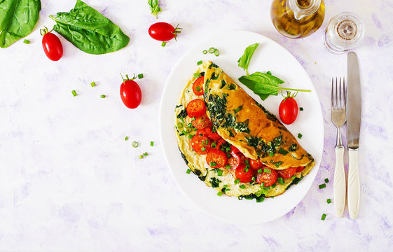 Omelette with tomatoes, spinach and green onion on white plate.  Frittata - italian omelet. Top view. Flat lay.