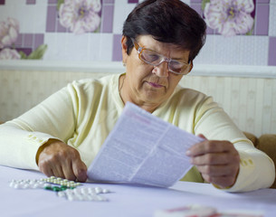 Senior woman reading information sheet of prescribed medicine sitting at table at home. Pharmacy,...