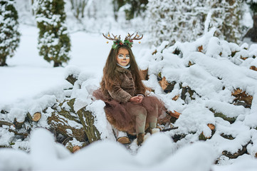 Fairy tale girl. Portrait a little girl in a deer dress with a painted face in the winter forest. Big brown antler © Serenkonata
