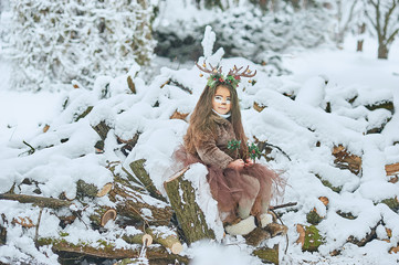 Fairy tale girl. Portrait a little girl in a deer dress with a painted face in the winter forest. Big brown antler