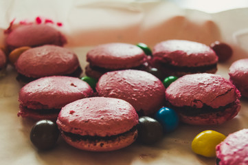 Dish with pink homemade macarons and colorful candies. Traditional french or italian cookies of different flavors in a wooden table. Natural lights.