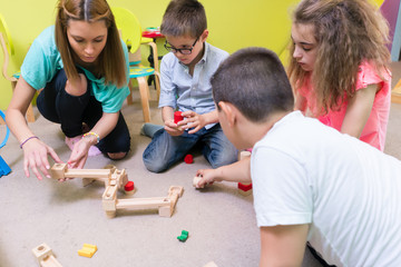 Low-angle view of a dedicated kindergarten teacher helping children with the construction of a...
