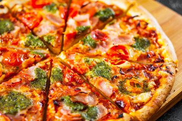 sliced Pizza with Mozzarella cheese, Ham, Tomatoes, pepper, Spices and Fresh Basil pesto sauce. Italian pizza.