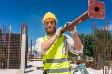 Full length of a blue-collar worker, wearing safety equipment while carrying a heavy metallic bar...