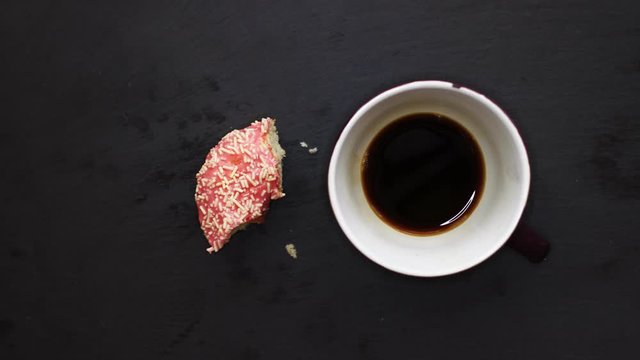 Eating pink donut and drinking a cup of coffee on dark background view from above, stop motion animation