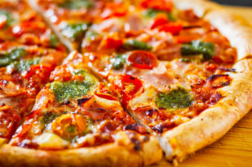 sliced Pizza with Mozzarella cheese, Ham, Tomatoes, pepper, Spices and Fresh Basil pesto sauce. Italian pizza.