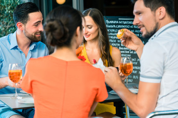 Cheerful young best friends toasting with a refreshing delicious summer drink while sitting together at table at a trendy restaurant outdoors