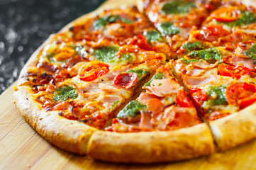 sliced Pizza with Mozzarella cheese, Ham, Tomatoes, pepper, Spices and Fresh Basil pesto sauce. Italian pizza.