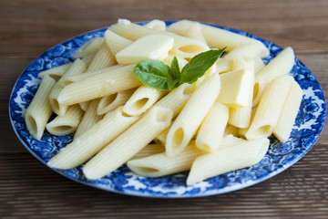 Cooked penne pasta with butter and cheese and basil in vintage beautiful plate on wooden table. Isolated.
