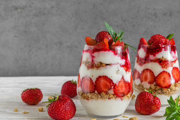 healthy strawberry yogurt parfait with granola, mint and fresh berries in glasses on white wooden table