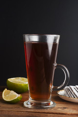 Glass Cup ofblack tea with lime, close up on rustic wooden background. Warm autumn or winter drinks.