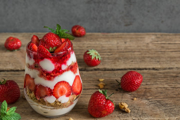 strawberry yogurt parfait with granola, mint and fresh berries in a glass on rustic wooden table. healthy breakfast
