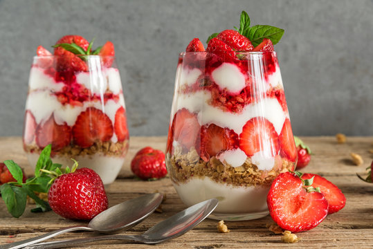 homemade strawberry yogurt parfait with granola, mint and fresh berries in glasses on rustic wooden table