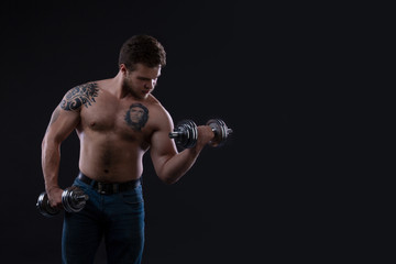 Plakat Muscular bodybuilder guy doing exercises with dumbbells over black background