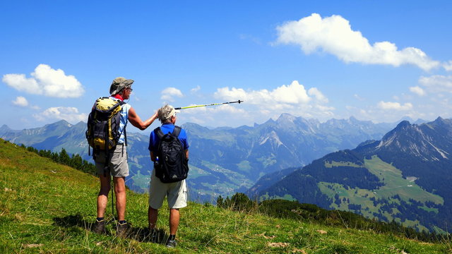2 Wanderer betrachten vom Hohen Frassen aus die herrliche Bergkette im sonnigen Bregenzerwald 