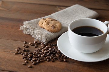 White cup of coffee with coffee beans and cookies on wooden table