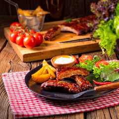 bbq spareribs on the plate with green salad and white sauce.