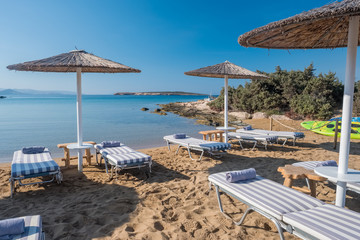 Umbrellas with sunbeds on beautiful sandy Santa Maria beach with turquoise sea water, Paros island,...