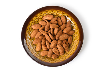 Close-up almond nuts on a brown plate, isolated on white background, view from above