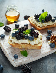 Fresh sweet Blackberry, Blueberry bruschetta, toast with cottage cheese, honey in a white board.