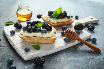Fresh sweet Blackberry, Blueberry bruschetta, toast with cottage cheese, honey in a white board.