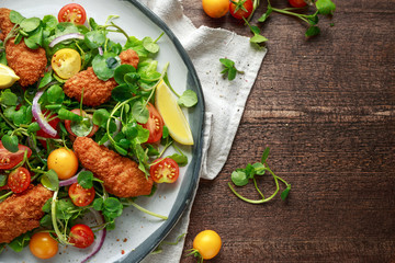 Fresh salad with chicken nuggets, cherry tomatoes, goat cheese and green vegetables in a rustic wooden table