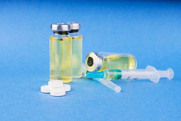 Group of vials with medicine, tablets and syringes on blue table.