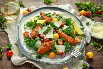 Fresh salad with chicken nuggets, cherry tomatoes, goat cheese and green vegetables in a rustic wooden table