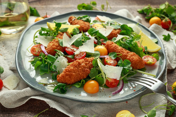 Fresh salad with chicken nuggets, cherry tomatoes, goat cheese and green vegetables in a rustic wooden table