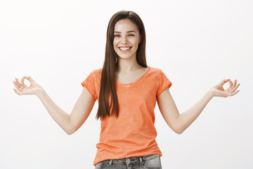 Staying positive and calm in urban hell. Positive joyful caucasian female student in orange t-shirt, spread hands with zen gesture and laughing, trying focus during meditation, being distracted