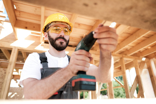 The man is a builder on the roof of a wooden frame house.