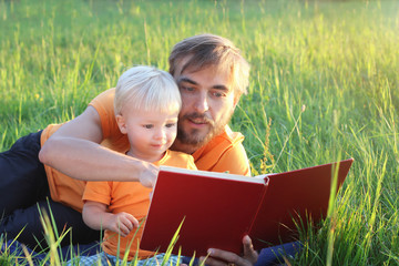 Father and his cute toddler son read book together in nature. Authentic lifestyle image. Parenting concept